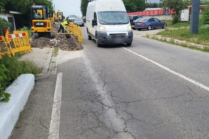 Road construction in progress: workers with yellow barriers and excavator along a cracked street as a white van passes by, Romania, Târgu Jiu.