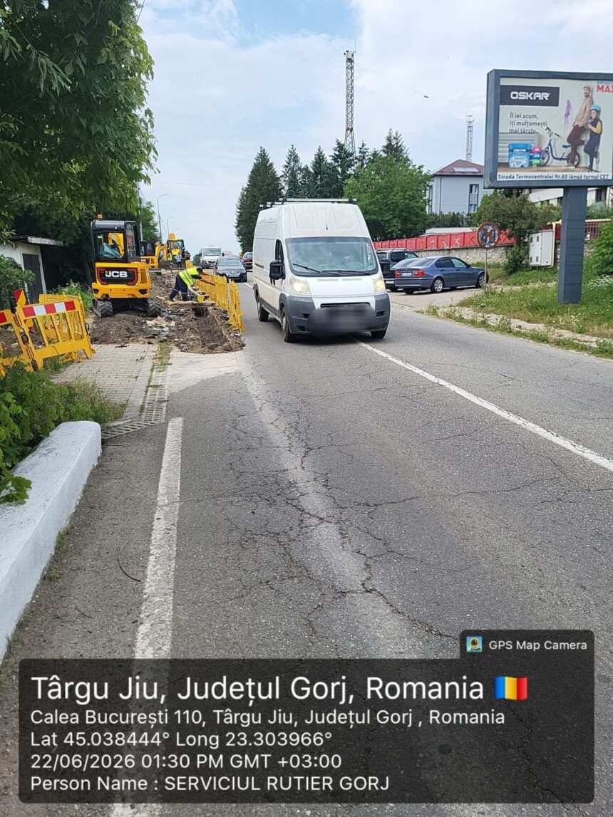 Road construction in progress: workers with yellow barriers and excavator along a cracked street as a white van passes by, Romania, Târgu Jiu.