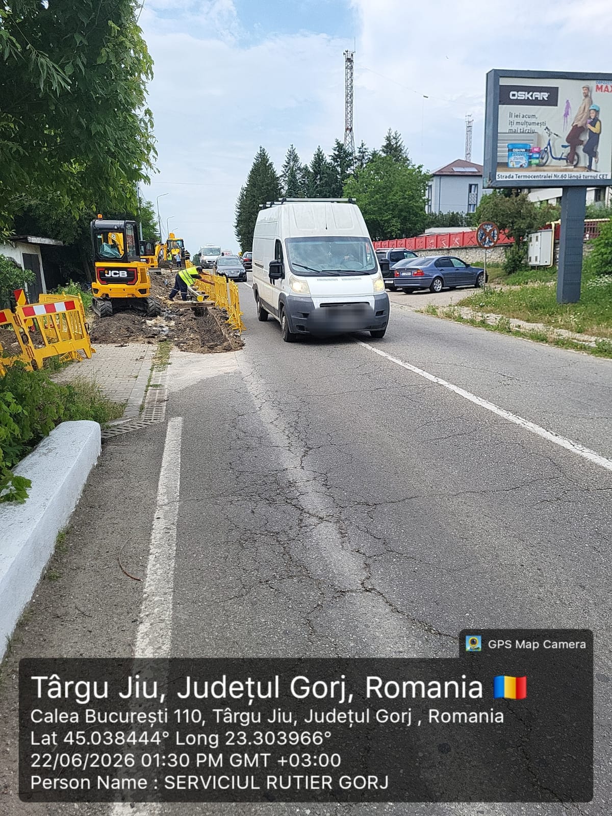 Road construction in progress: workers with yellow barriers and excavator along a cracked street as a white van passes by, Romania, Târgu Jiu.