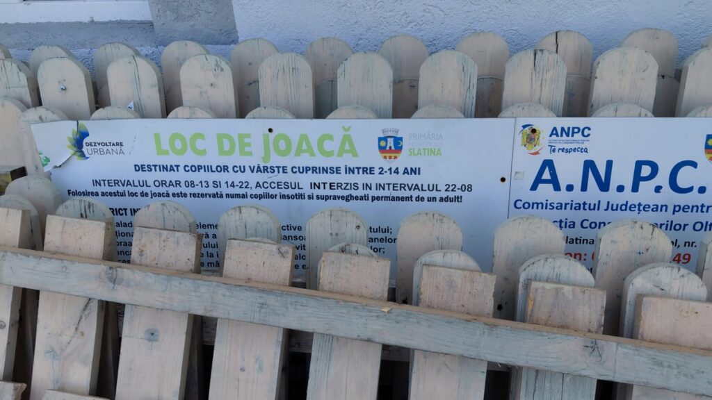 Sign reading 'LOC DE JOACĂ' behind a weathered wooden fence, indicating a children's play area in Slatina, Romania.