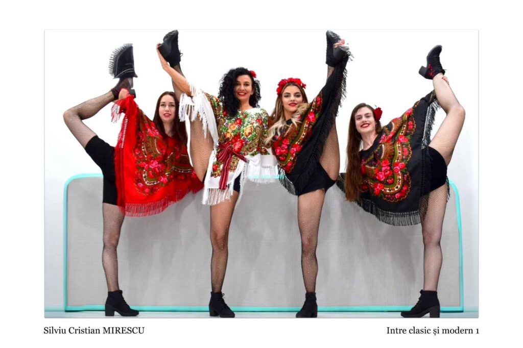 Five dancers in colorful traditional costumes perform high-leg kicks in a row against a light backdrop, smiling at the camera.