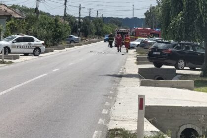 Emergency responders and a police car on a street, with a fire truck in the distance and people in red uniforms approaching a blocked road area.
