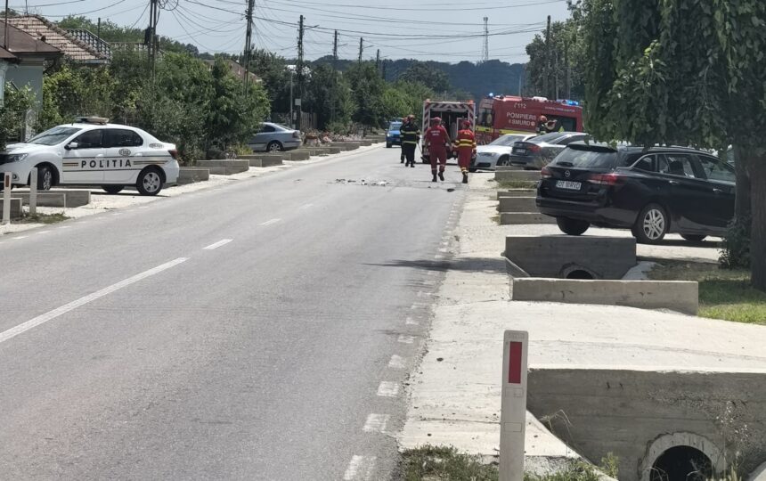 Emergency responders and a police car on a street, with a fire truck in the distance and people in red uniforms approaching a blocked road area.