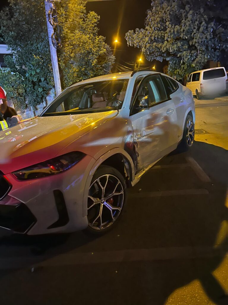 accident basarabilor 2 - Jurnalul Olteniei – Știri din Craiova și Oltenia White sedan with visible front-end damage parked on a dimly lit street at night; a person in a helmet stands near the driver's side.