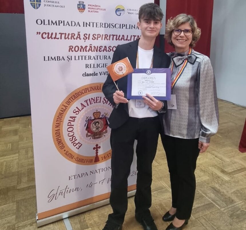 Young man in a blazer holds a diploma and orange flag while standing with a smiling woman at an academic award ceremony, with a banner in the background.