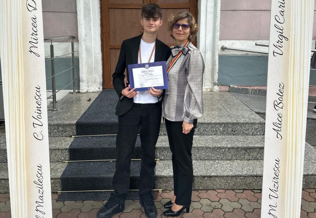 Student in a black blazer and white shirt holding a diploma, posing with a woman on steps outside a building.