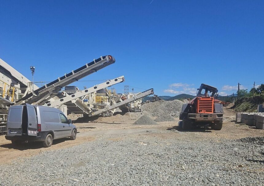 Construction site with multiple conveyor belts, a grey van, and an orange excavator under a clear blue sky.