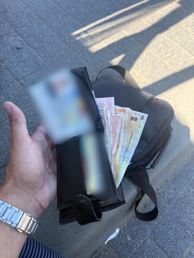 Wallet held in a left hand with Turkish lira banknotes fanned out of a black wallet on a street surface?