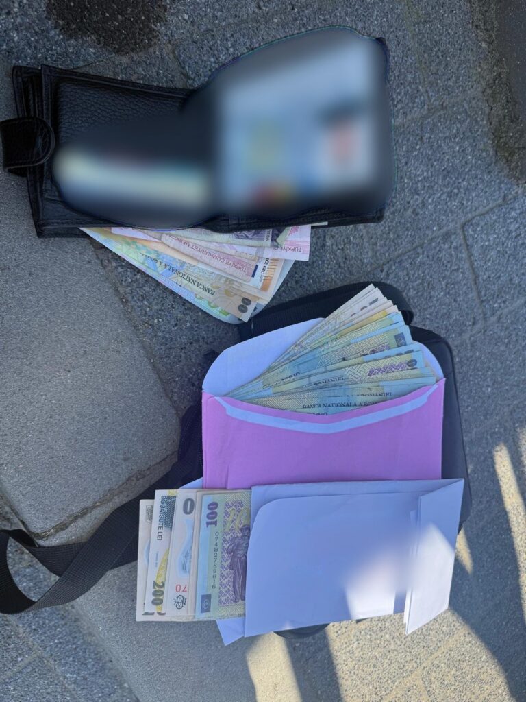 Black wallet on the ground with cash fanned out beneath, and a pink envelope filled with more money under it on a pavement surface.
