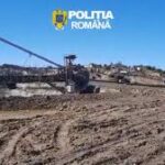 Open-pit mining site with large excavators and conveyor towers on barren ground, blue sky above; Romanian Police (Politia Romana) logo visible in the sky.
