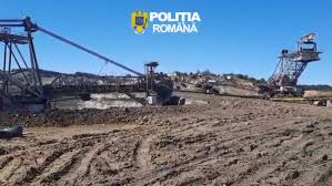 Open-pit mining site with large excavators and conveyor towers on barren ground, blue sky above; Romanian Police (Politia Romana) logo visible in the sky.