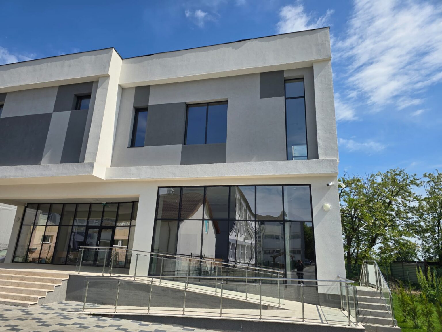 centrul multifunctional bals - Jurnalul Olteniei – Știri din Craiova și Oltenia Modern two-story building with large glass windows and a ramp railing, under a bright blue sky.