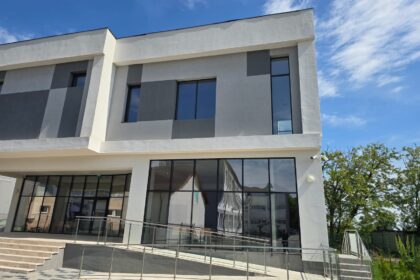 Modern two-story building with large glass windows and a ramp railing, under a bright blue sky.