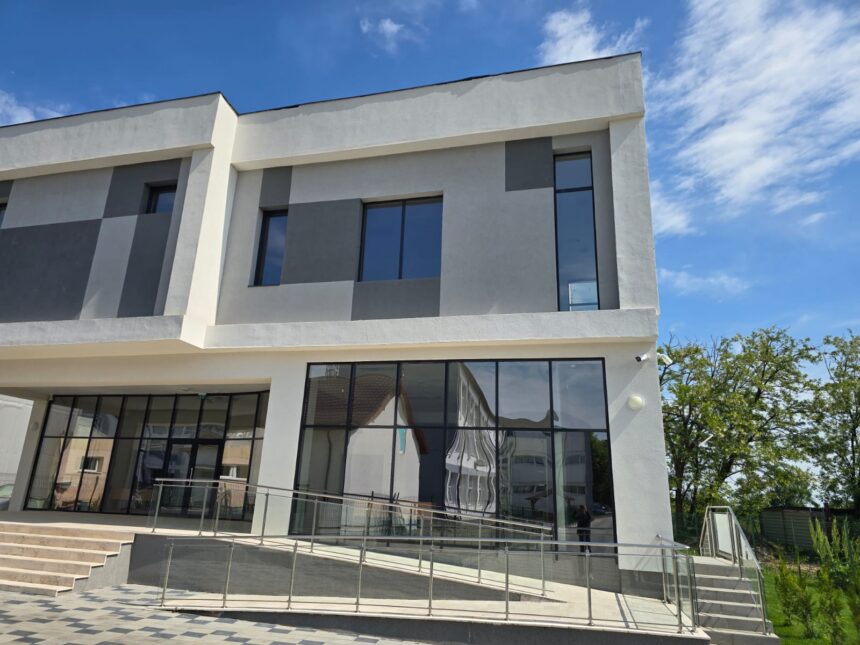 Modern two-story building with large glass windows and a ramp railing, under a bright blue sky.