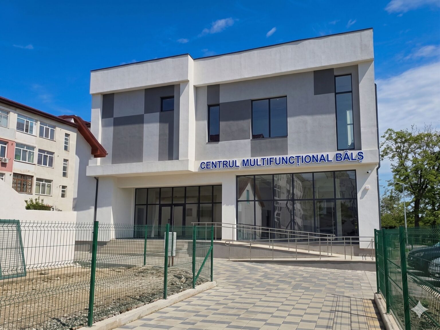 centrul multifunctional bals - Jurnalul Olteniei – Știri din Craiova și Oltenia Modern gray-and-white building with large glass windows and a blue sign reading CENTRUL MULTIFUNCTIONAL BALS under a clear blue sky.