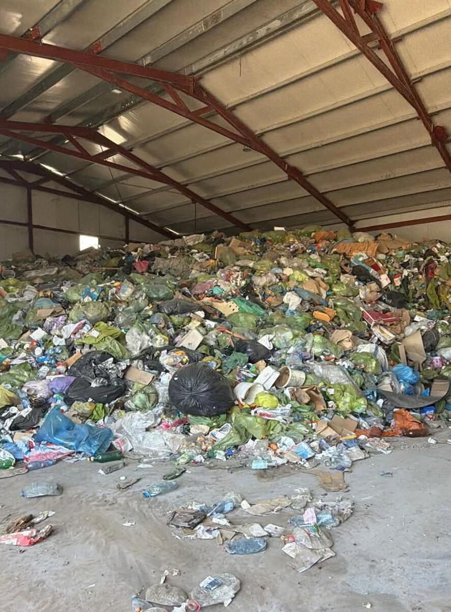 deseuri - Jurnalul Olteniei – Știri din Craiova și Oltenia Large pile of mixed trash and garbage bags piled inside an industrial warehouse with metal support beams above.