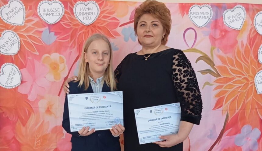 Girl and woman stand together, each holding diplomas, in front of a pink floral backdrop with heart shapes.