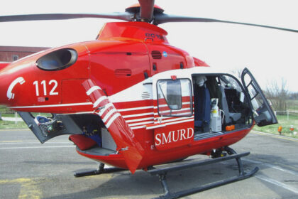 Red emergency rescue helicopter with open side door on a helipad, SMURD markings and 112 number visible outside the cockpit gear inside