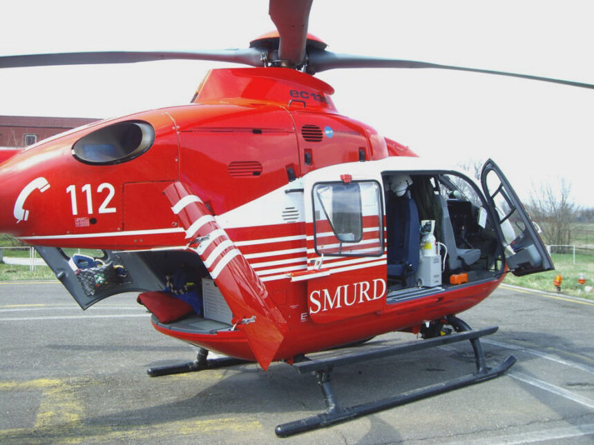 Red emergency rescue helicopter with open side door on a helipad, SMURD markings and 112 number visible outside the cockpit gear inside