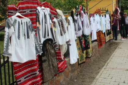 Row of traditional white shirts with black embroidery and red fabrics hung on a fence at an outdoor market.