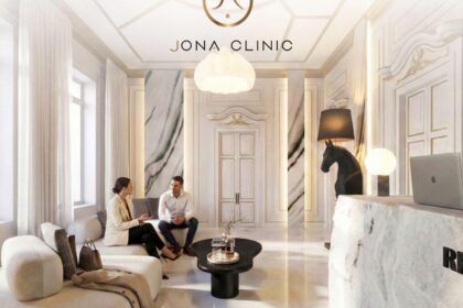 Luxurious white marble clinic lobby with two people seated on a sofa, chatting under the JONA CLINIC logo.