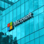 Microsoft logo on a blue glass office building façade, sign mounted on the exterior glass wall