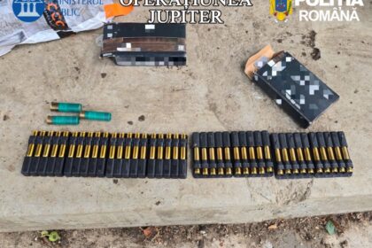 Row of black cartridge holders with gold-tipped bullets and a few green shotgun shells on a concrete surface, with opened boxes nearby and 'OPERATIUNEA JUPITER' and 'POLIŢIA ROMÂNĂ' branding