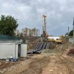 Construction site with a dirt road, crane and excavator, and stacks of materials on both sides.