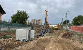 Construction site with a dirt road, crane and excavator, and stacks of materials on both sides.