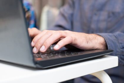 Close-up of hands typing on a laptop keyboard on a white desk nearby.