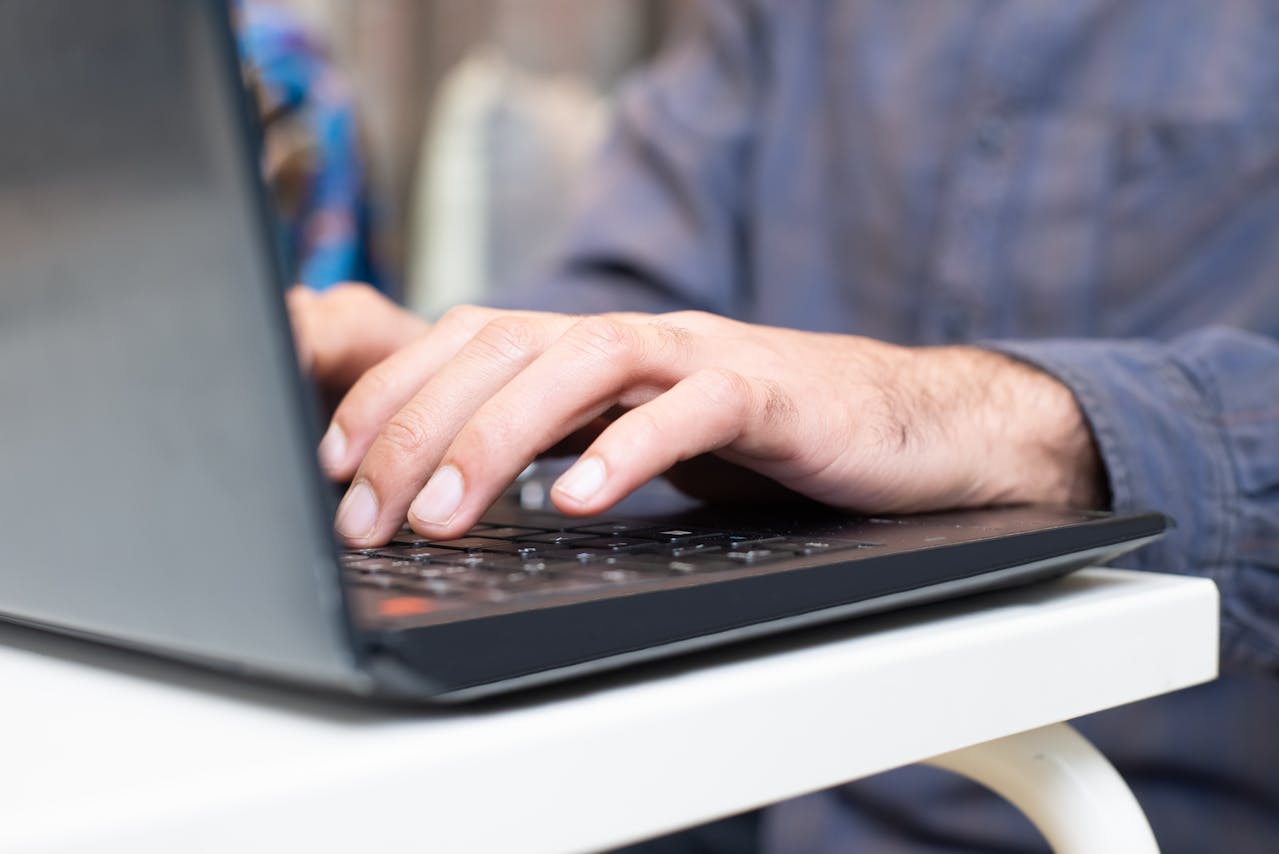 Close-up of hands typing on a laptop keyboard on a white desk nearby.