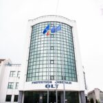 Front view of a white office building with a curved glass facade and three flagpoles in front, flags fluttering outside.