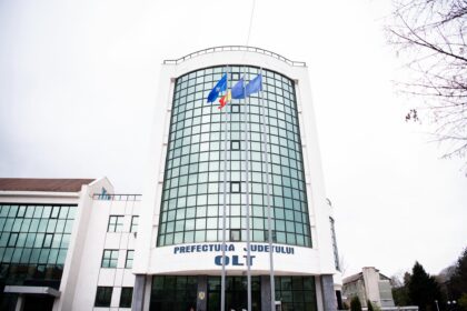 Front view of a white office building with a curved glass facade and three flagpoles in front, flags fluttering outside.