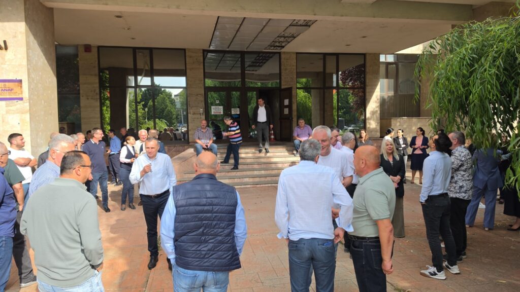 Crowd of people gathered outside a glass-fronted building entrance with steps. Trustworthy, informal gathering.