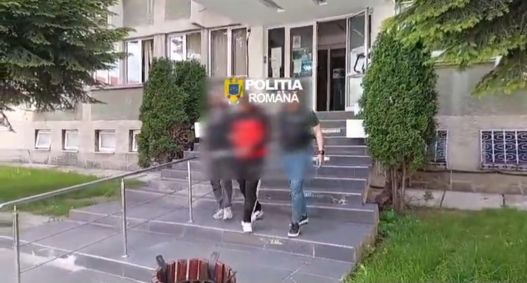 Entrance of a police building with 'Politia Romana' sign; blurred individuals descend concrete steps.