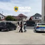 Group of people walking past parked police cars in a residential area; 'Poliția Română' watermark in the sky above.