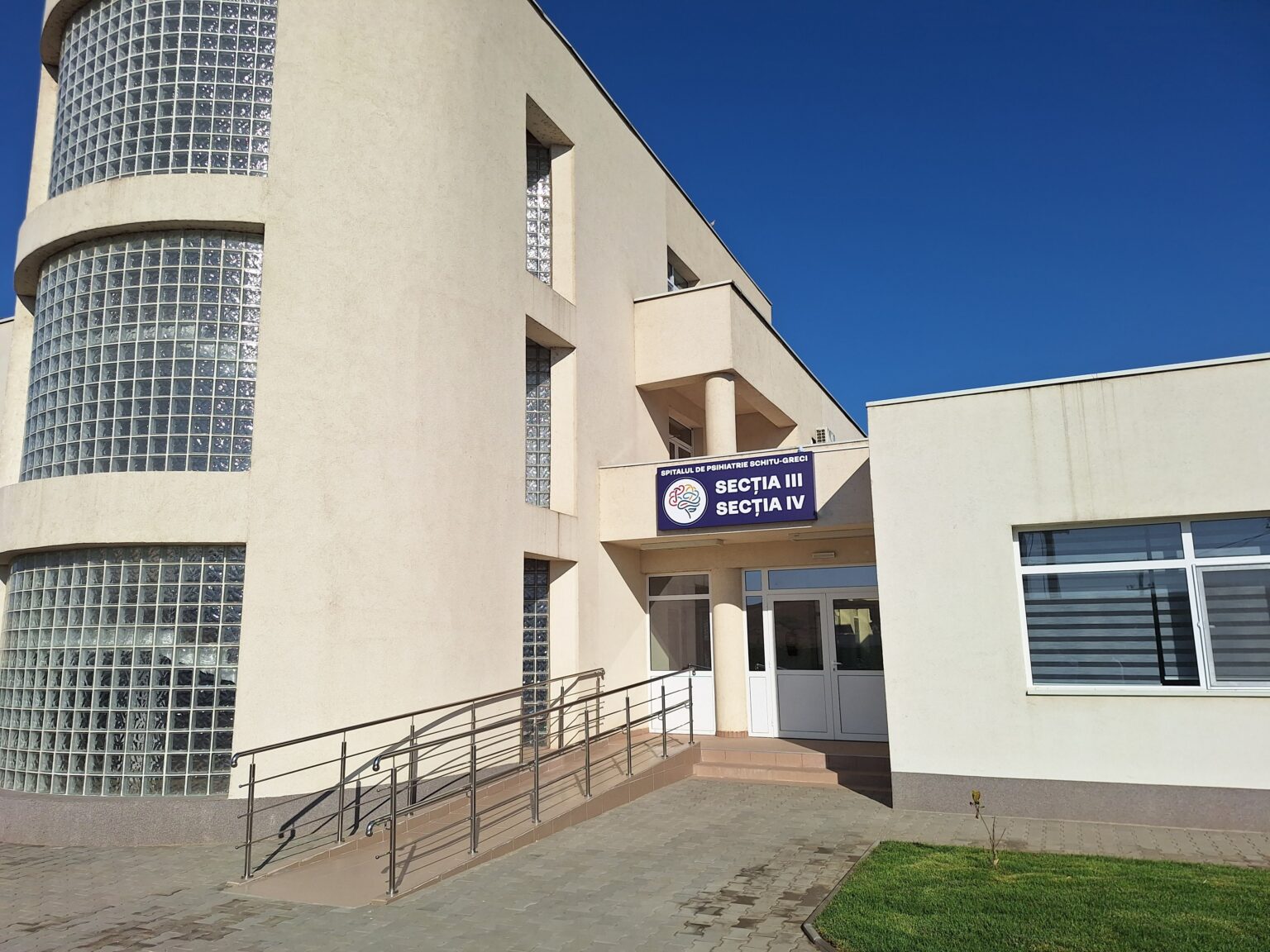 Beige modern hospital building with curved glass block windows and a ramp to the entrance.
