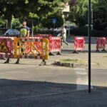 Construction site on a city street with red-and-white barriers and a yellow gate blocking traffic