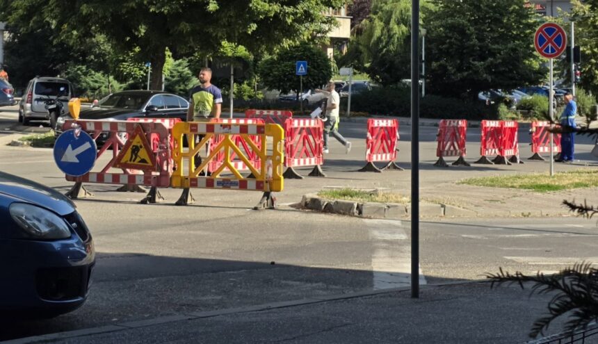 Construction site on a city street with red-and-white barriers and a yellow gate blocking traffic