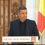 Man in a dark blazer speaks at a podium labeled 'Partidul Social Democrat' with Romanian and EU flags in the background.