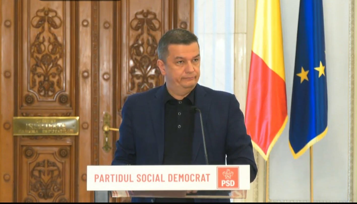 Sorin Grindeanu cere ”comisie de criză” pentru PNRR - Jurnalul Olteniei – Știri din Craiova și Oltenia Man in a dark blazer speaks at a podium labeled 'Partidul Social Democrat' with Romanian and EU flags in the background.