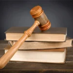 Wooden gavel resting on a stack of old books on a wooden table, suggesting a legal or judicial context.