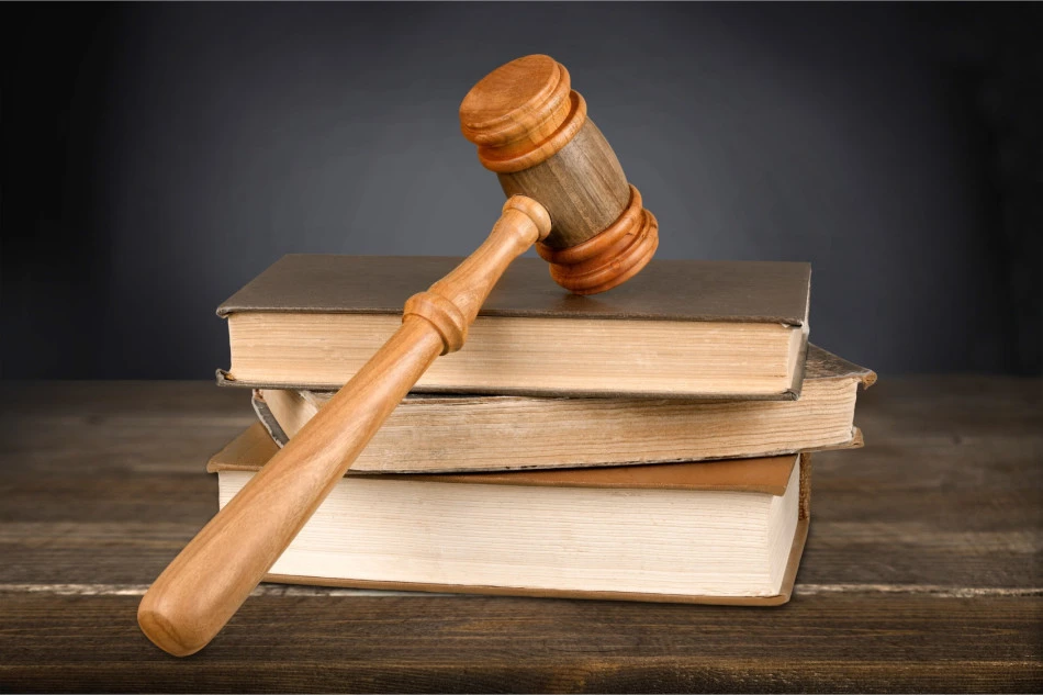Wooden gavel resting on a stack of old books on a wooden table, suggesting a legal or judicial context.