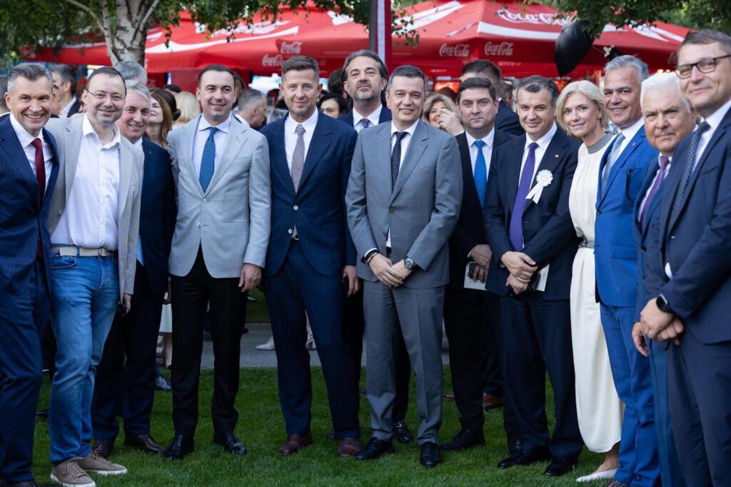 Group of professionally dressed people posing for a photo at an outdoor event under red Coca-Cola tents.