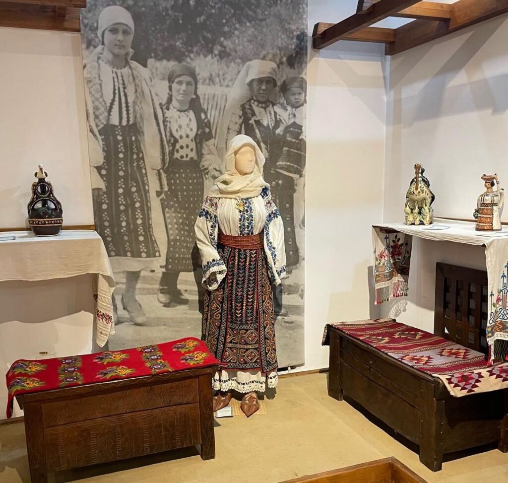 Mannequin in a traditional folk costume with embroidered blouse and red patterned skirt in a museum display with woven textiles nearby
