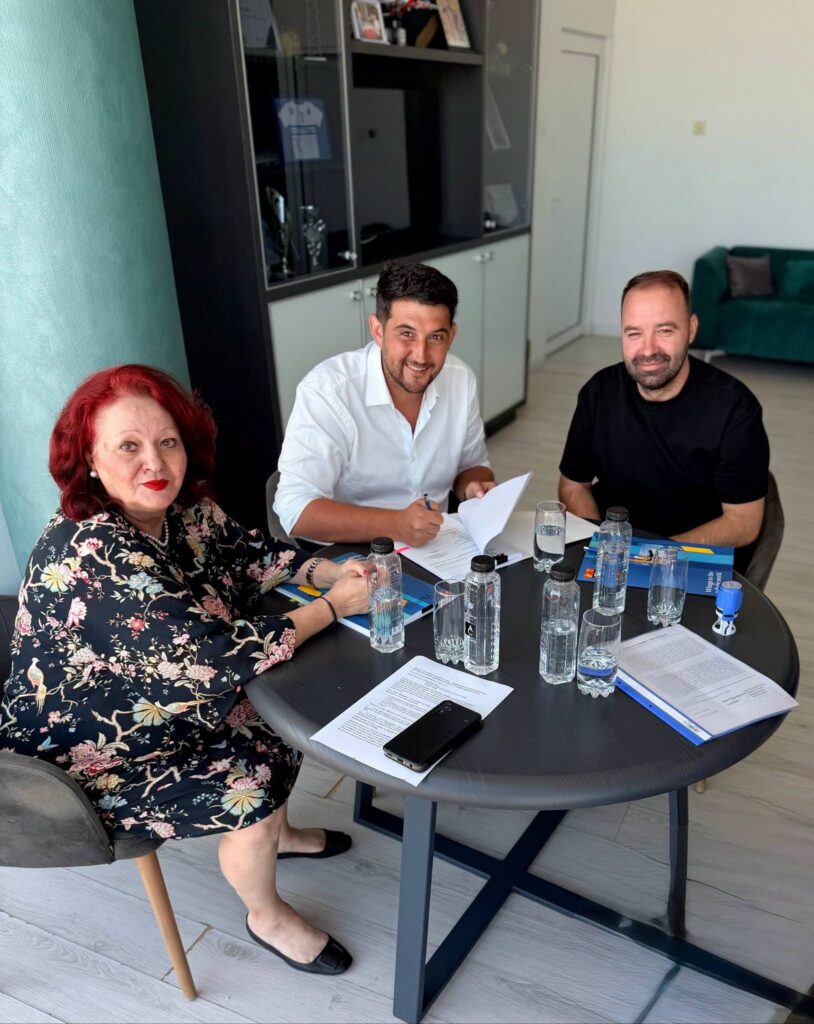 - Jurnalul Olteniei – Știri din Craiova și Oltenia Three adults sit around a round table with papers and water bottles, posing for a photo during a meeting; woman in floral dress on left, man in white shirt center, man in black shirt on right, in a modern office.