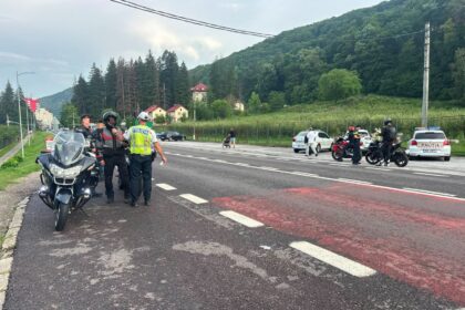 Police checkpoint on a two-lane road in a hilly, green landscape; officers with reflective vests and motorcycles are stopped as patrol carsmarked POLITIA observe nearby.