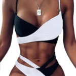 Woman in a black and white bikini with an asymmetric top and wrapped bottoms, wearing a pendant necklace.