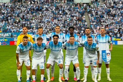 Soccer team in white-and-blue striped kits posing for a pre-match group photo on the field with a packed stadium behind them