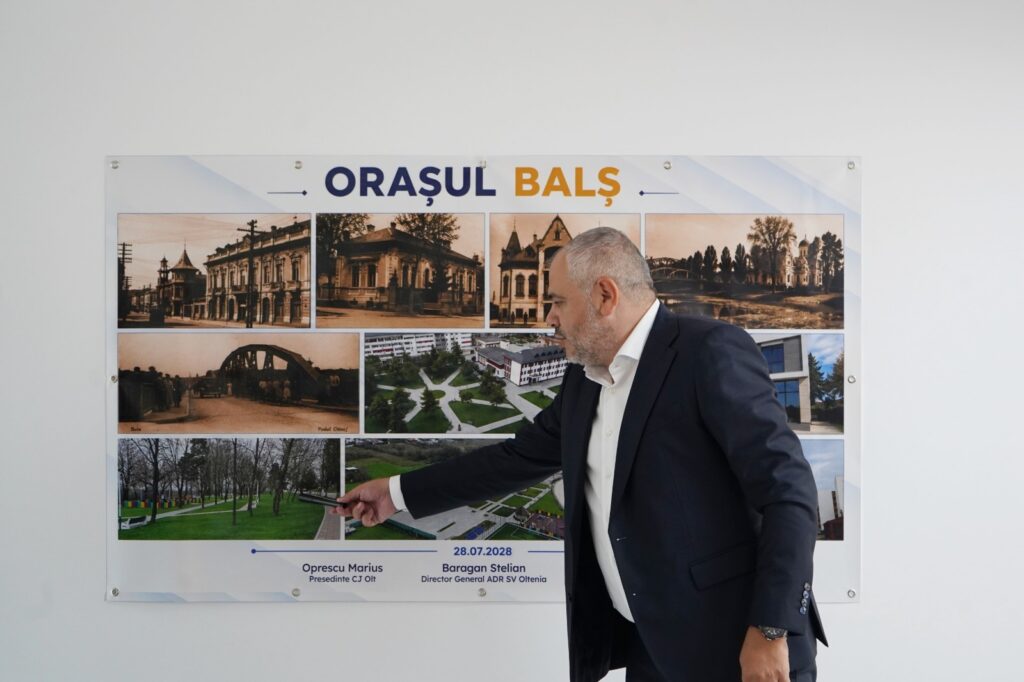 Man in a navy suit points at a large poster titled Orașul Bals, a collage of town photos.